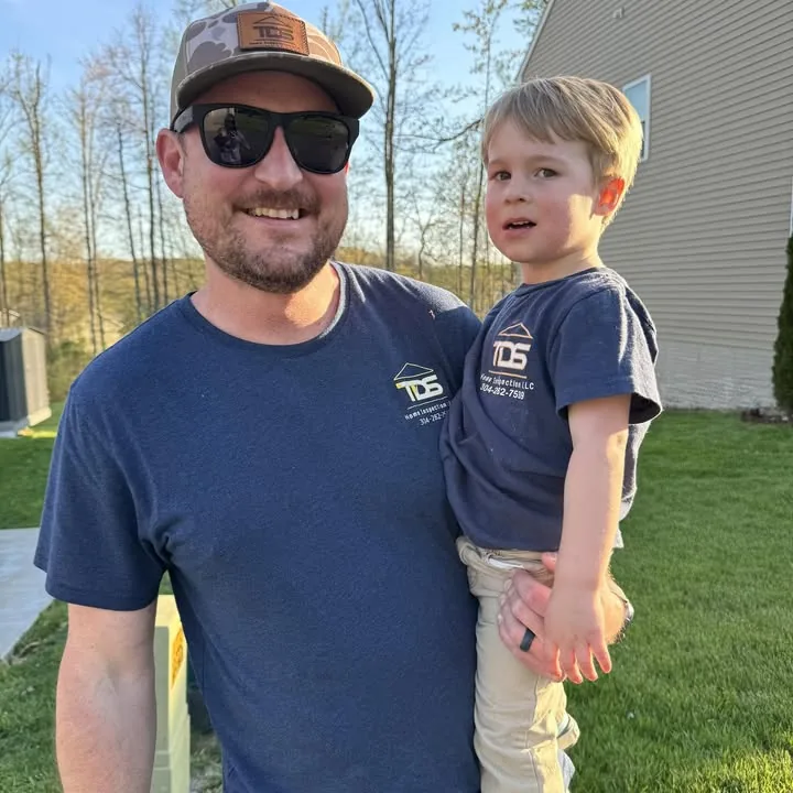 Tyler Sherman in a TDS Home Inspection shirt and cap, holding his son Brooks, who wears a matching TDS shirt